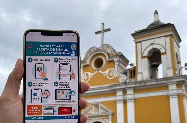 Teléfono móvil mostrando una notificación del sistema de alerta de terremotos frente a una iglesia en Guatemala.