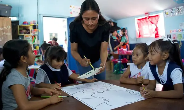 Profesora enseñando técnicas de pintura a un grupo de niñas de primaria en un salón de clases